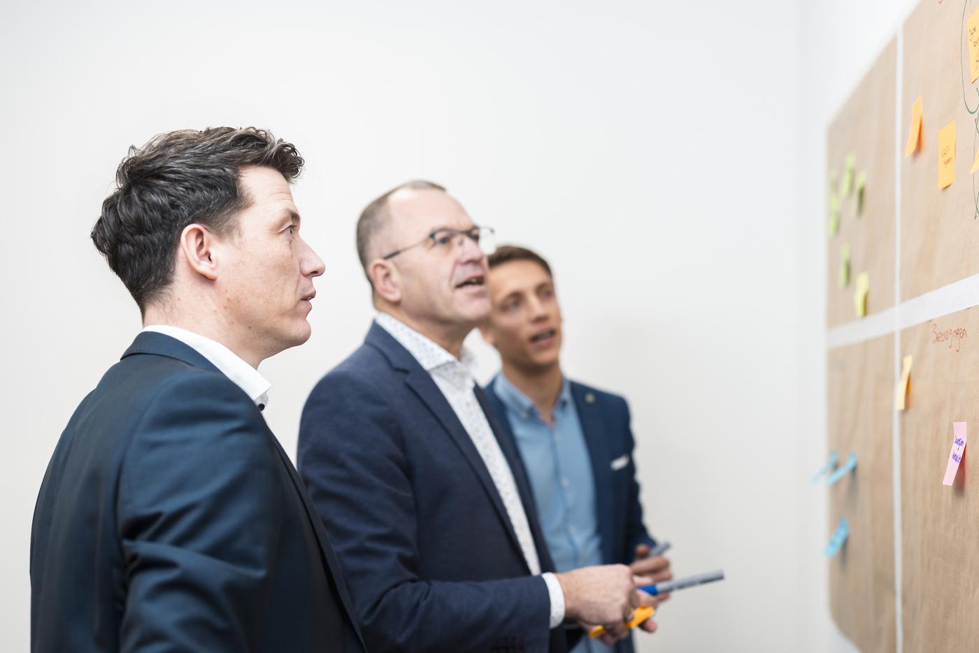 Drie collega's van TNP Groep overleggen bij een prikbord met post-its