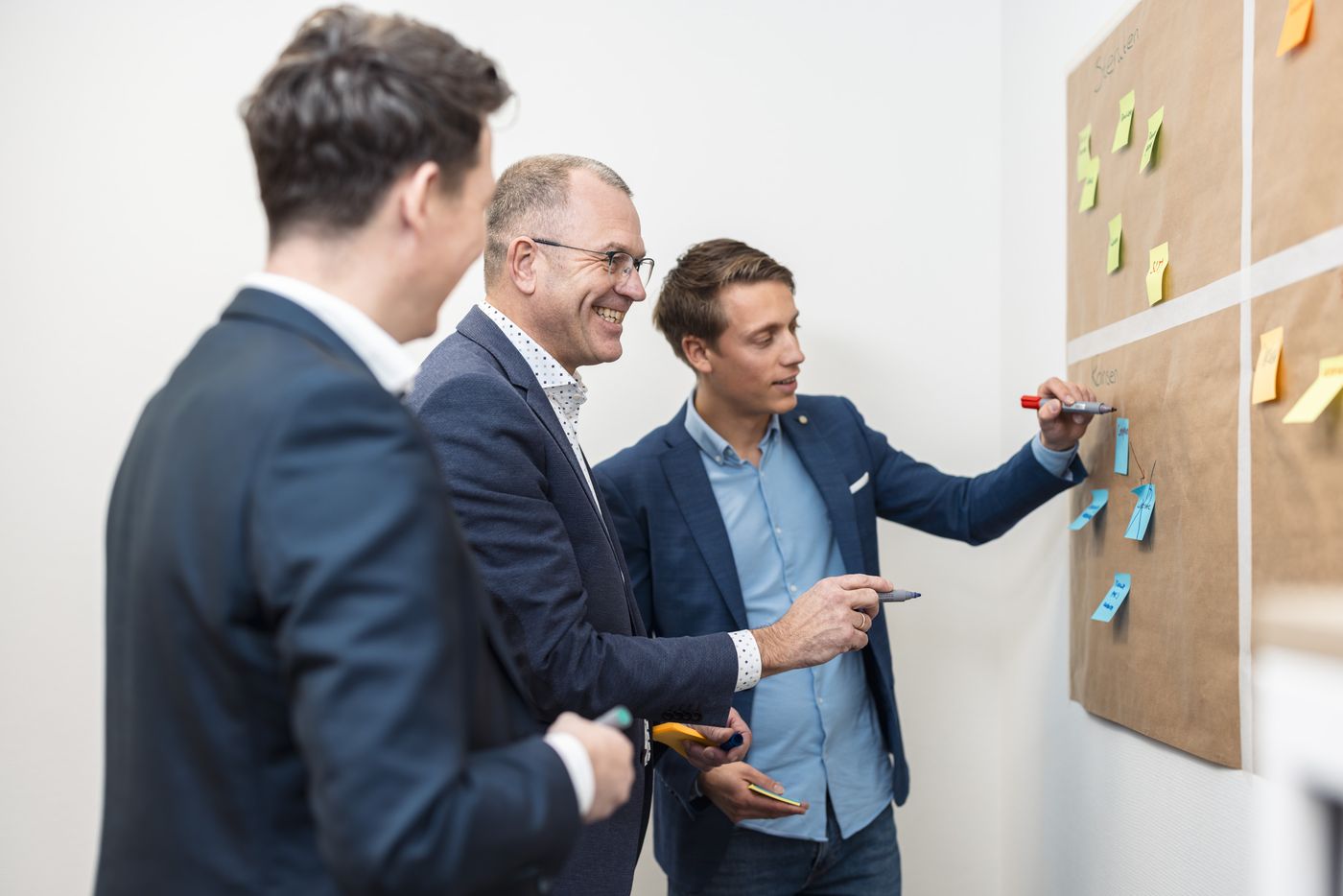Drie collega's bespreken de uitkomsten bij een prikbord met post-its