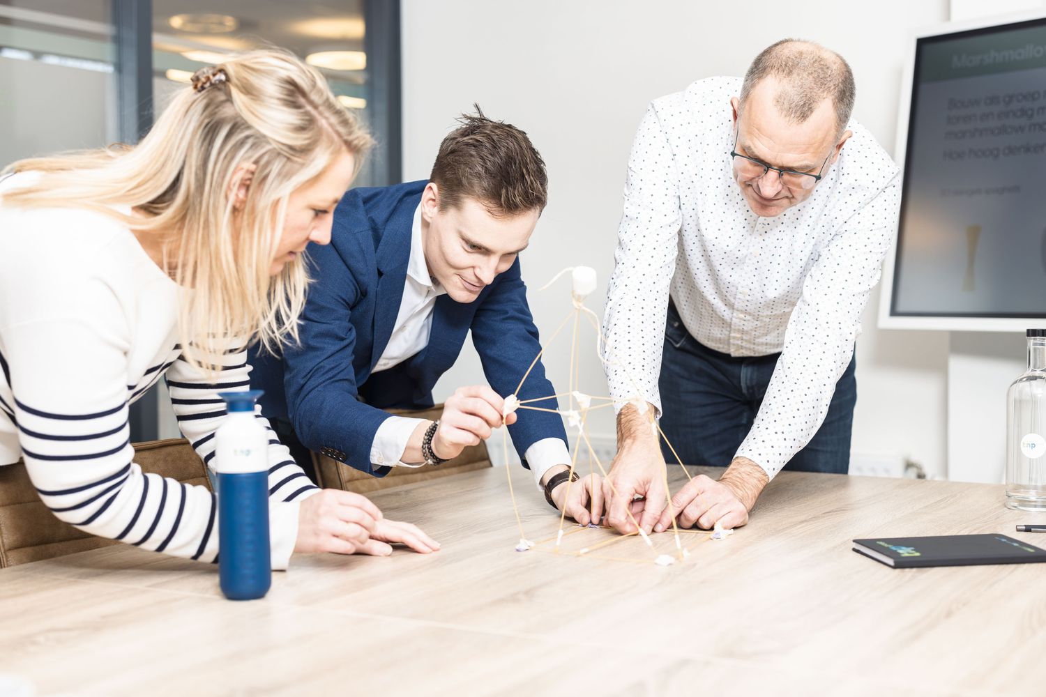 Een team bouwt samen aan een toren van spaghetti en marshmallows op tafel